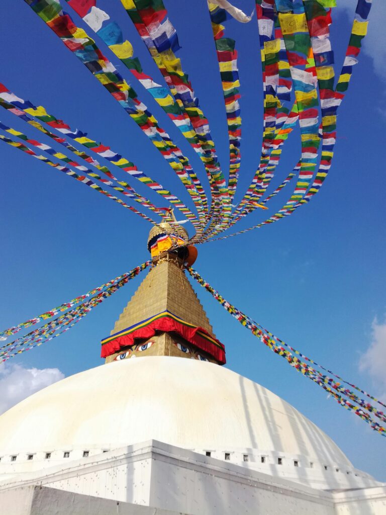 Vibrant prayer flags adorn the iconic Boudhanath Stupa under a clear sky in Kathmandu.